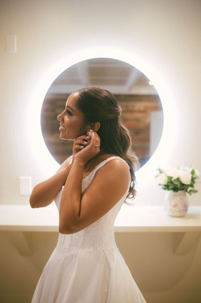 Bride fastening her earring beside an illuminated mirror in the Deer Park Villa Bridal Cottage